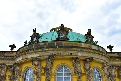 Ancient royal palace with yellow walls, tall windows, antique statues and decor on the facade and a large green dome. Historical architecture. Germany, Potsdam, Sans Souci, August 2022.