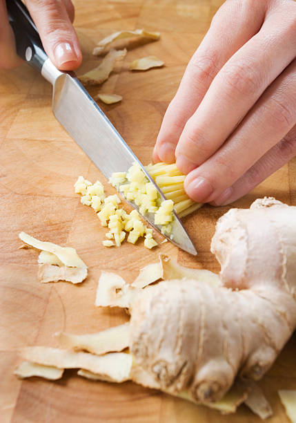 Fine chopping ginger. "Finely chopped ginger on a wooden chopping board.To see more of my food related images, click on the banner." ginger stock pictures, royalty-free photos & images