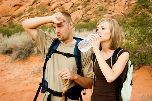 A couple drinks water and wipes sweat on a hot desert hike.Click to see more models-