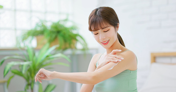 skin care concept - asian confident woman is applying lotion and moisturizer on her arm