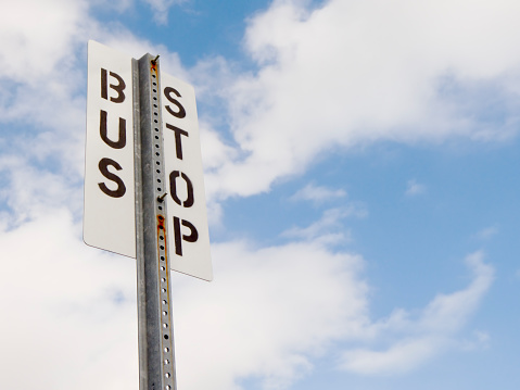 A bus stop sign against the blue sky and white clouds, horizontal version.