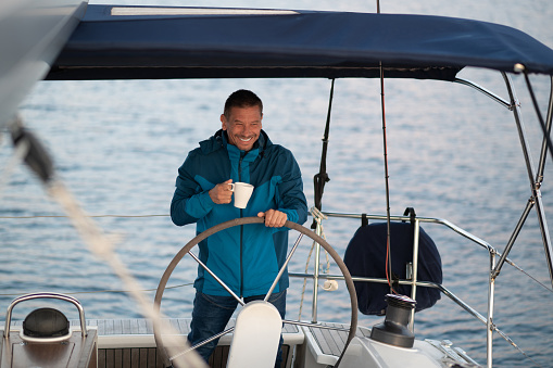 Man on a yacht. Man in blue jacket on the yacht having coffee and looking contented