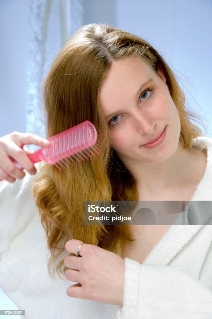 young women brushing hair head and shoulders shot of a young blond woman in white bathrobe brushing her hair with a pink hairbrush smiling at the camera Adult Stock Photo