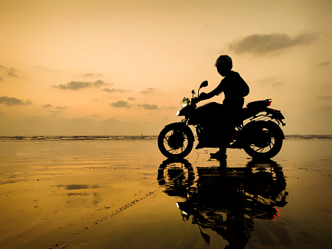 Silhouette image of motorcyclists on the beach and enjoying the beautiful view of sunset.