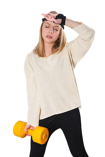 Exhausted Blonde Cute Fitness Little Girl with Dumbbells Photo of a young blonde sport fitness girl with dumbbells, she is exhausted while lifting hand weights. Dressed in modern sports clothing and headband. Isolated on white background. Barbell stock pictures, royalty-free photos & images