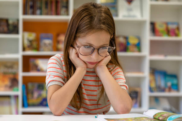 istock Little bored girl reading book in school library. 1724057278