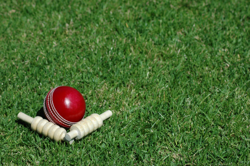 Red leather cricket ball and bails arranged on cricket pitch