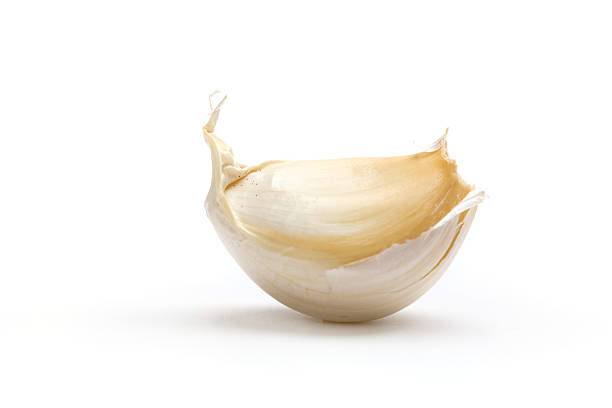 Half of a garlic bulb with peel sitting on white table stock photo