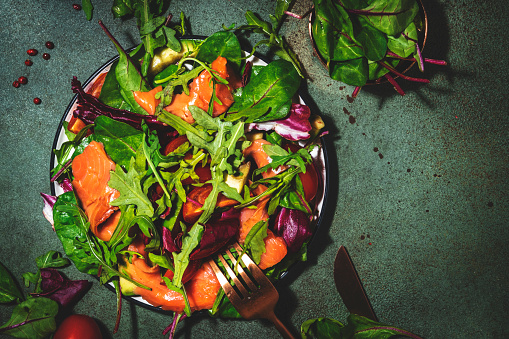 Salted Salmon salad with arugula, beet leaves, radicchio, tomatoes, lemon and olive oil dressing. Rusty green background, top view, hard light
