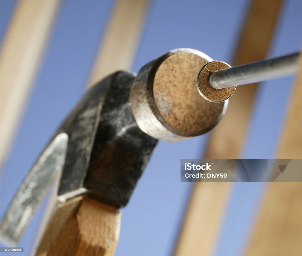 Hammer and Nail Hammer pounding nail. Construction framing in background with blue sky. Focus is on nail head Building - Activity Stock Photo