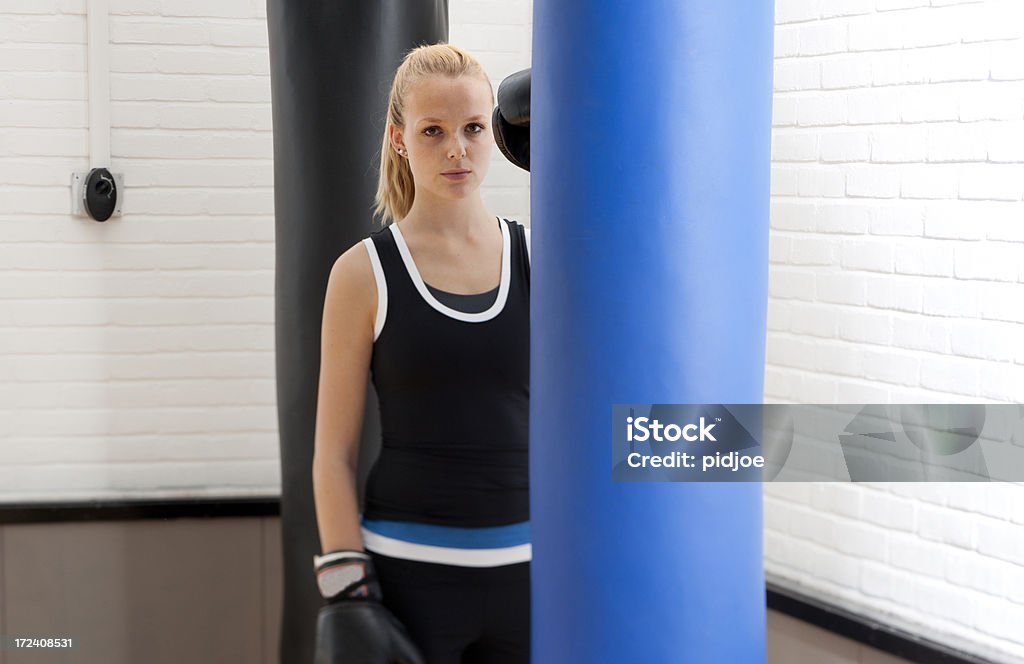 female boxer in gym "young woman with boxing gloves standing bewteen a blue and black punching bag in gym looking at the camera, shot with tilt shift lens focus on the face" 20-24 Years Stock Photo