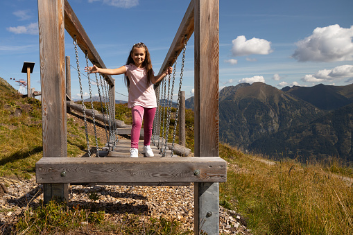 Smiling girl in pink deftly moves on suspended logs to train balance. High quality photo