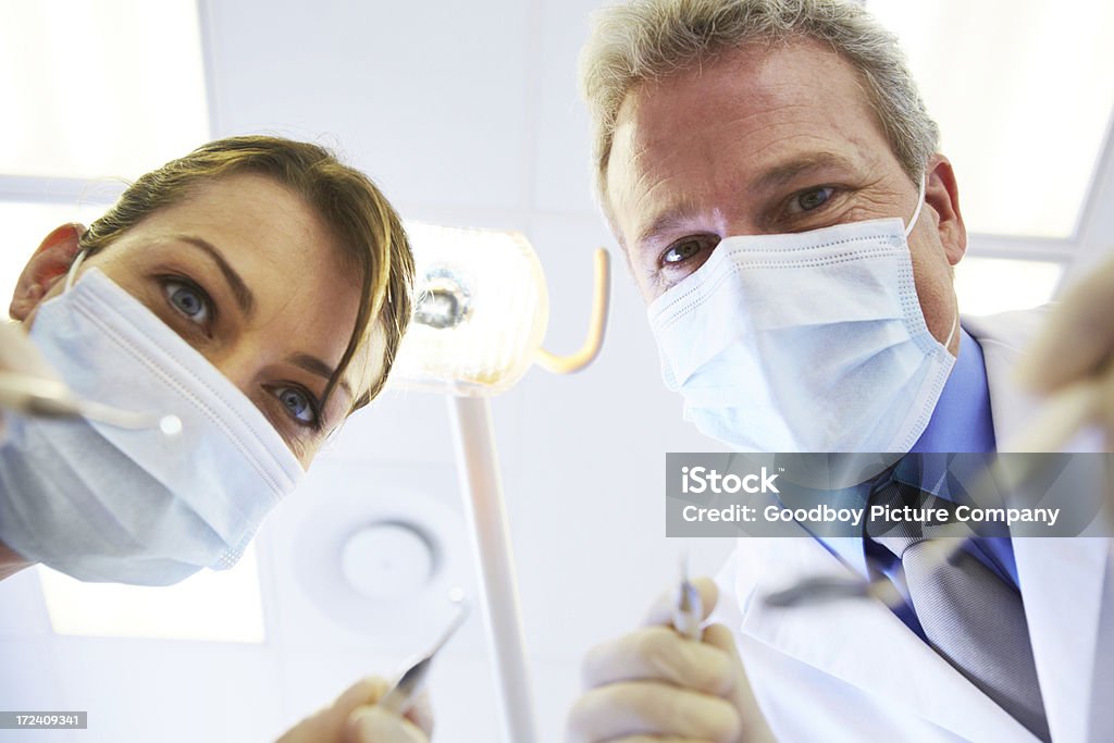 Let's fix these teeth Low view of a masked dentist and his assistant holding instruments above you Adult Stock Photo