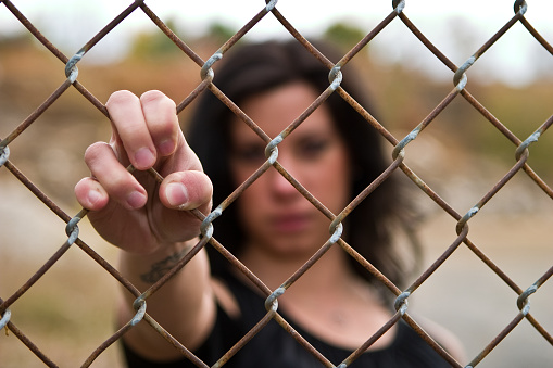 young woman gripping fence, shallow depth of field