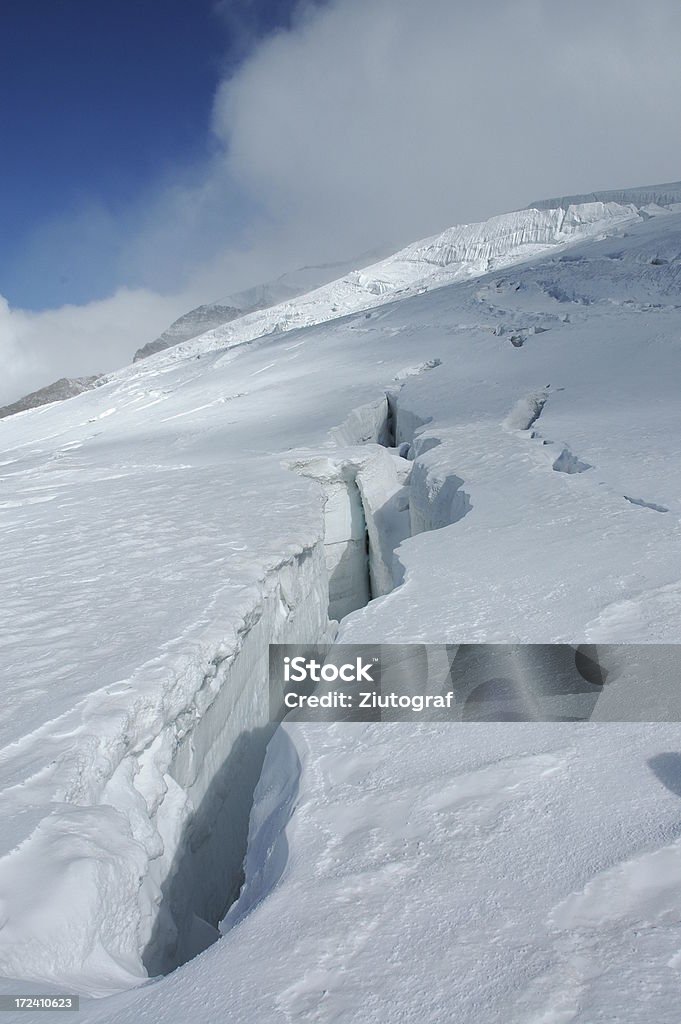 Crevasse in Alps A long crevasse in European Alps covered by fresh snow. Clouds and blue sky on the horizon. Cold Temperature Stock Photo