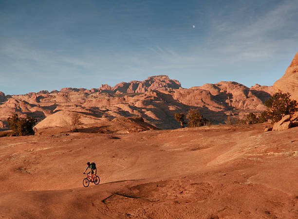 Mountain Biking in Desert Mountain biker rides on the slickrock bike trail in Moab Utah. Dunes and desert in background. slickrock trail stock pictures, royalty-free photos & images