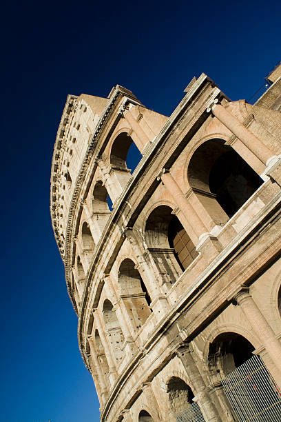 Low angle view of Coliseum at dusk in Rome, Italy. Image taken with zoom in zoom out technic. Full frame image. Lights shining from windows to the outside. Horizontal composition. Outdoors. It also known as the Flavian Amphitheatre. Coliseum is an oval amphitheatre in the centre of the city of Rome, Italy. Built of concrete and sand. It is the largest amphitheatre ever built. It was used for gladiatorial contests and public spectacles such as mock sea battles, animal hunts, executions, re-enactments of famous battles, and dramas based on Classical mythology.