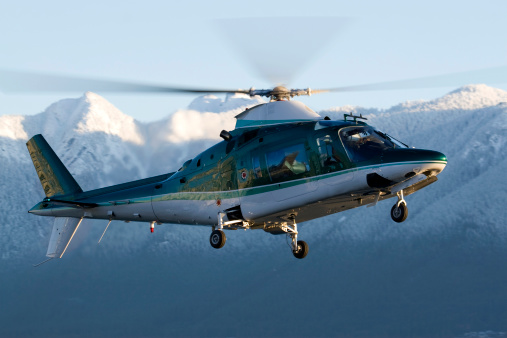 A corporate helicopter lit up by the morning sun.  Snow capped mountains in the background.