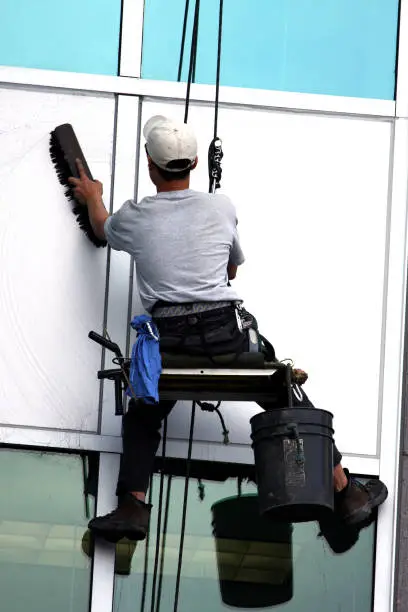 A window washer hangs high up on a building while he cleans it