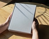 Hands holding closed book mockup on wooden table