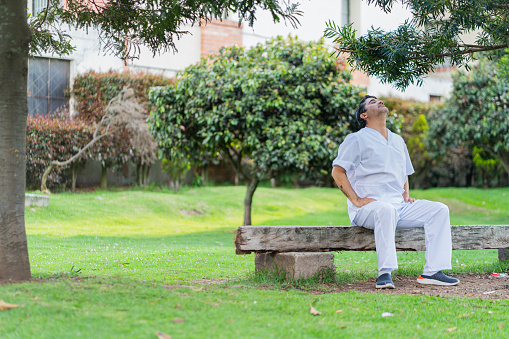 Latino nurse from Bogota Colombia, between 40 and 49 years old, takes a break in the park after finishing his shift at the clinic wearing his uniform