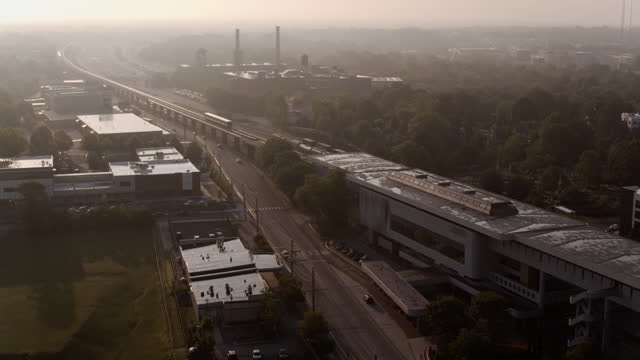 Train departing from railroad station in the morning. Row houses and parking lots adjacent to railroad. Morning rush into Downtown, Atlanta, Georgia. Aerial footage with panning camera motion
