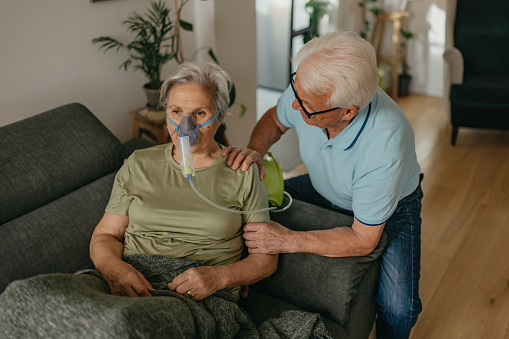 Senior man assisting senior woman during process of medical inhalation