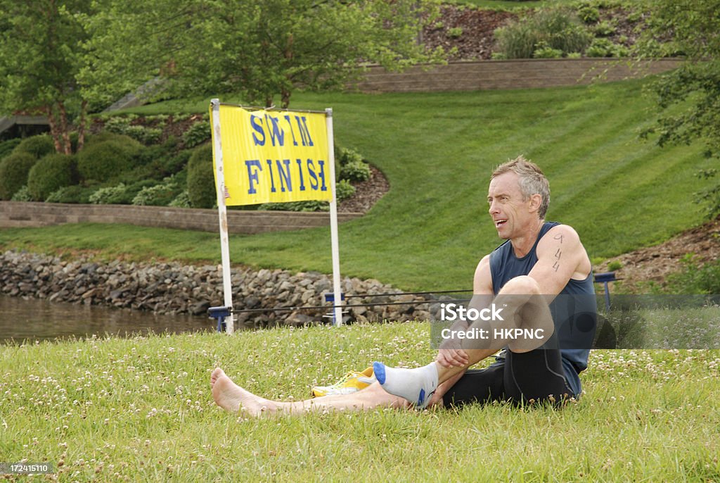 After The Triathlon 2 "Fifty something man stretches after completing a triathlon.  Pictured behind the competitor is the swimming start / finish line and the lake.  All logos, brand, & icons removed.See other related images here:" Active Lifestyle Stock Photo