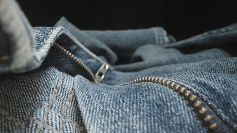 The camera glides across blue denim pants, passing through a metallic zipper. Texture. Dolly slider extreme close-up.