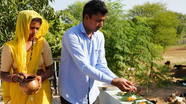 Photo of Hindu religious man with his wife offering food placed on a green leaf during a Hindu Ritual in the month of Sharada. Pitru paksha concept.
