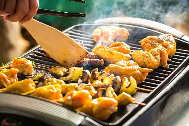 Barbeque electric grill with cevapcici, chicken wings and chicken skewers.