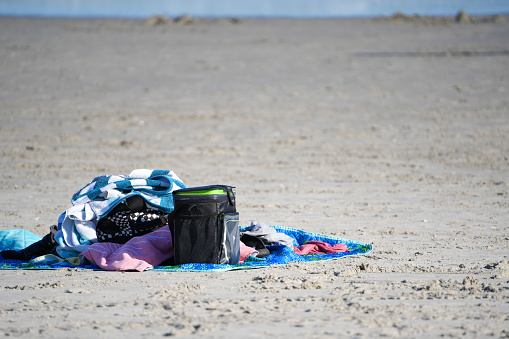 Beach picnic setup with towels, blankets, and a cooler on the sandy shore