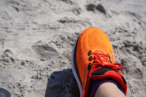 Bright orange running shoe on the beach sand