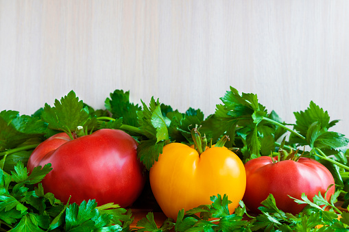 Fresh tomatoes on a wooden table with fresh parsley and celery greens. Red and yellow vegetables.