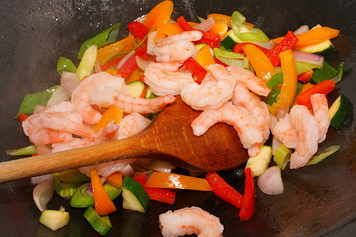Vegetable and king prawn stir fry in a wok pan with ladle. King prawns, spring onions, red onions, zucchini and red and yellow bell pepper. Steaming hot!