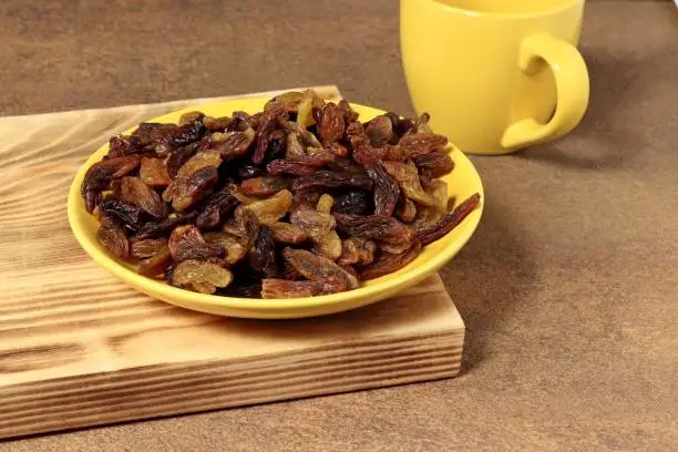 Photo of Yellow saucer filled with raisins and a cup.