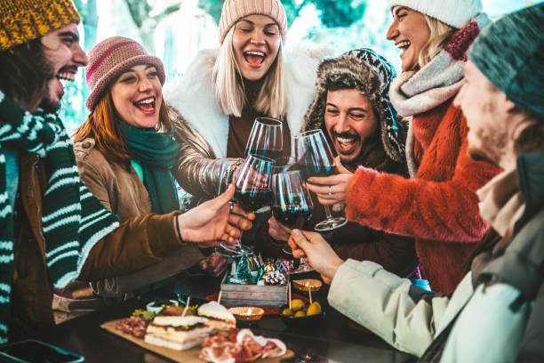 happy friends group toasting red wine dining at restaurant terrace - young people socializing drinking and eating food sitting outside at winery bar table - winter season - dinner lifestyle concept - apres ski fotos imagens e fotografias de stock