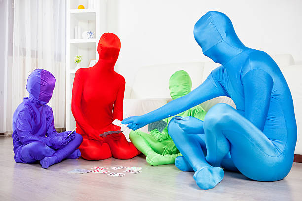 Color Family Playing cards at home. Color Family in zentai bodysuits with two children playing cards at home and having fun together. Beauty of diversity and stop racism concept. zentai lifestyle stock pictures, royalty-free photos & images