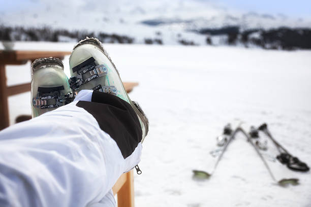 Skier with feet up and skis in background Skier relaxing with her feet up in a mountain restaurant.  Defocussed skis and mountains in background. apres ski stock pictures, royalty-free photos & images