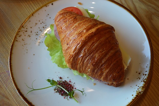 Croissant sandwich with green salad and salmon, close-up. Healthy breakfast concept.