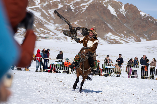 Bayan-Olgii Province, Mongolia - September 30, 2023: Ethnic Kazakh eagle hunter riding with golden eagle tethered to arm at a local Golden Eagle Festival.