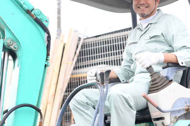 A construction worker wearing a hard hat and safety vest directs heavy machinery on a bustling city street under a bright sun with clear skies.