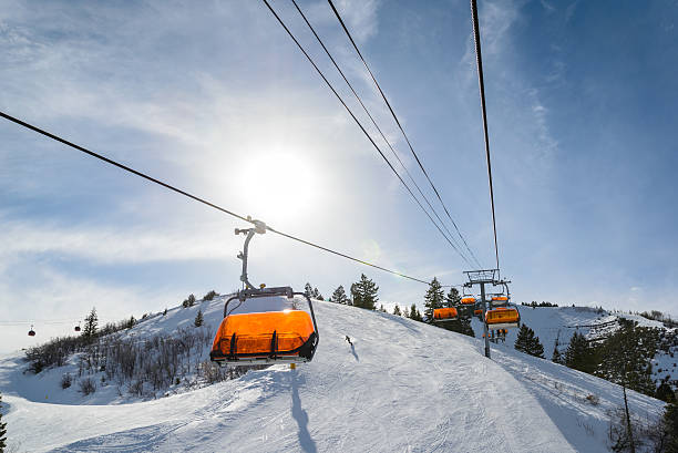 Riding Chairlift in Winter "Park City, Utah orange covered ski lifts with sun on sunny day.  Riding up chairlift late in the afternoon.  Captured as a 14-bit Raw file. Edited in 16-bit ProPhoto RGB color space." ski lift photos stock pictures, royalty-free photos & images