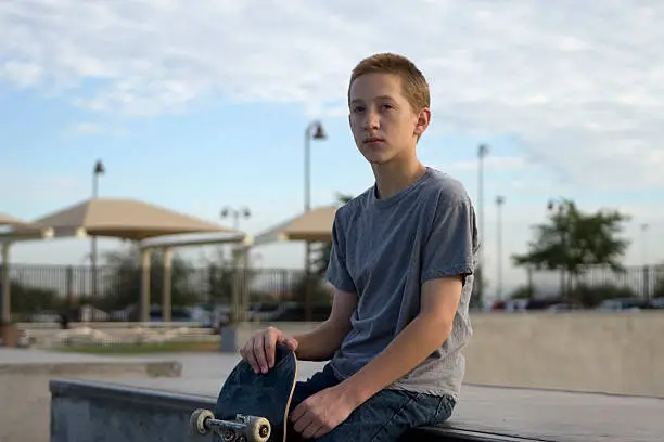 Young male teen sitting with skateboard