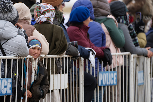 Bayan-Olgii Province, Mongolia - October 1, 2023: A child looks in the other direction from among a crowd of spectators standing behind a fence at the Ulgii Golden Eagle Festival.