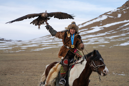 Bayan-Olgii Province, Mongolia - October 1, 2023:  Aimuldir D., an ethnic Kazakh female eagle hunter and winner of her local Golden Eagle Festival, rides with a golden eagle tethered to her arm.