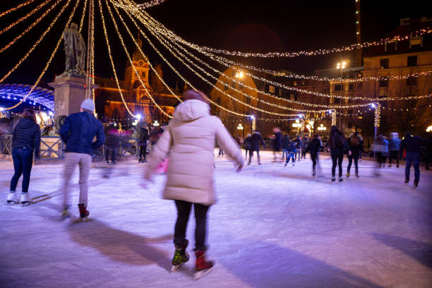 Detailed shot of women's legs in white figure skating skates on cold ice arena in the dark with blue light. A woman slides on the ice, splashing particles of sparkling ice into the camera. Close up