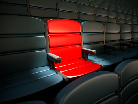 Spotlit red seat standing out among regular black seats.