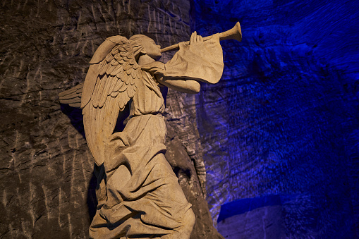 Zipaquira, Colombia - 04 12 2019: angel sculpture and giant cross at catholic cathedral of Zipaquira is built into the tunnels of an underground salt mine and artfully illuminated in colorful light.