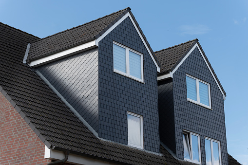 Closeup of attic windows and brick chimneys on house roof top covered with ceramic shingles. Tiled covering of building.